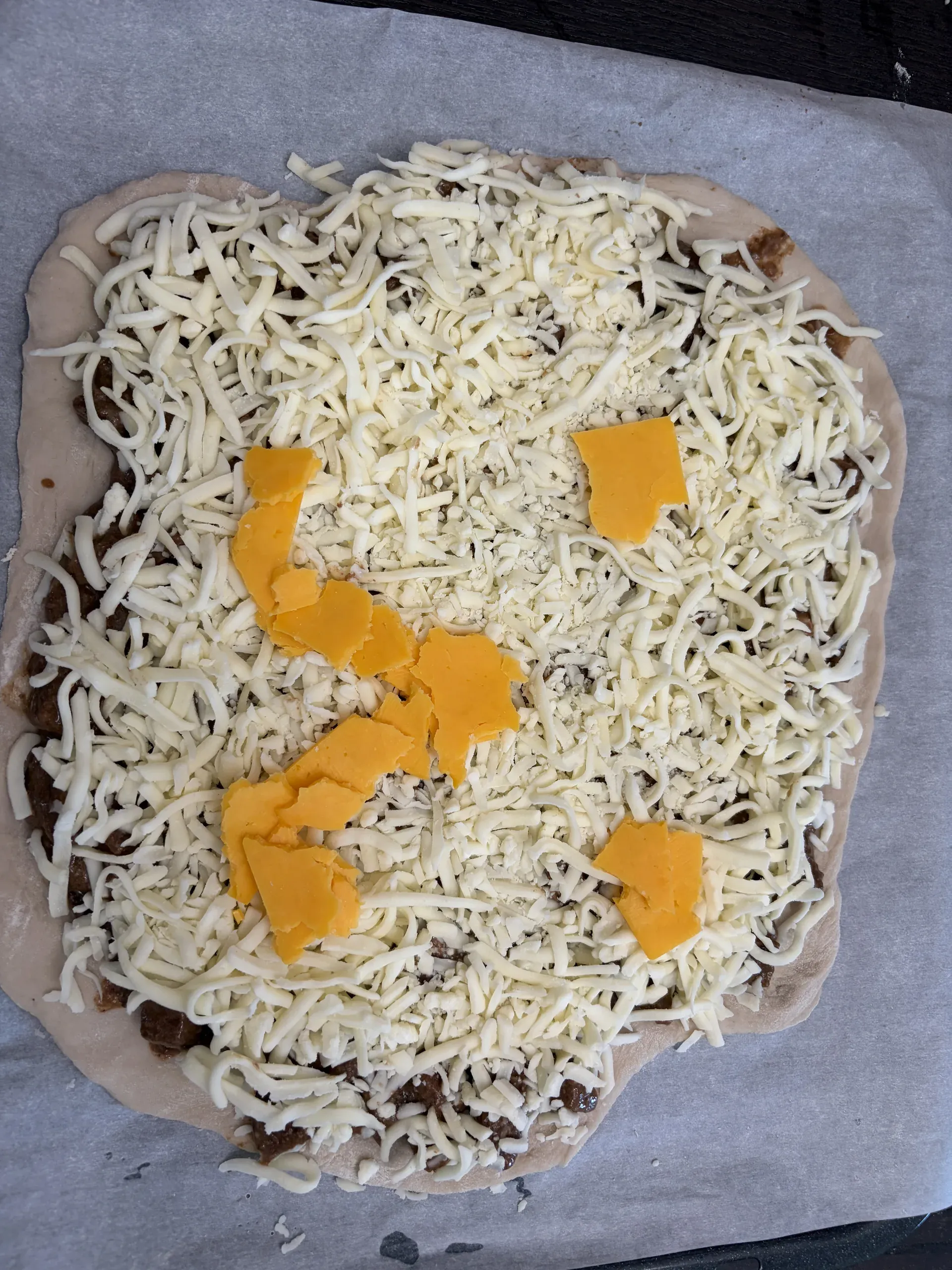 Unbaked pizza dough topped with beef, shredded mozzarella, and a cheddar cheese smiley face